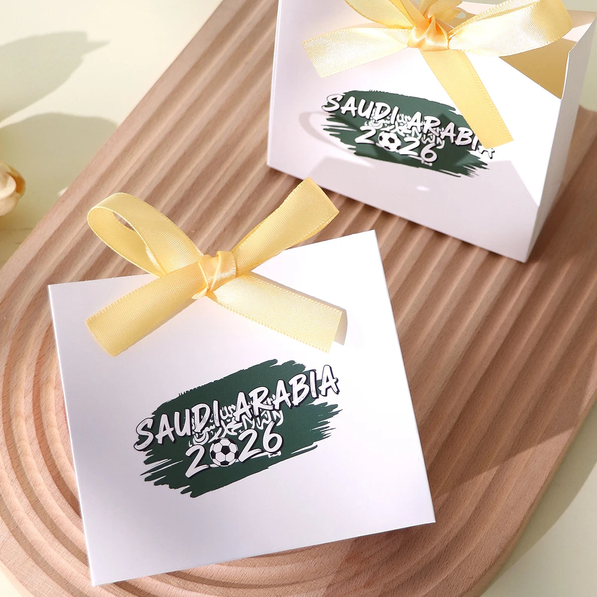Saudi Arabia 2026 Football-Themed Gift Box, Simple White Box with Green Football Print, Adorned with a Delicate Yellow Satin Ribbon Bow, Featuring a Clean and Elegant Design The Box Has Clear Printing and a Fine Texture, Maki Qme