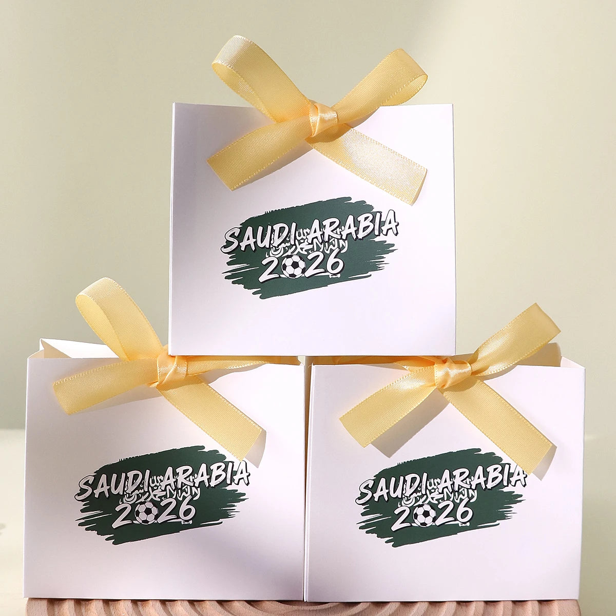 Saudi Arabia 2026 Football-Themed Gift Box, Simple White Box with Green Football Print, Adorned with a Delicate Yellow Satin Ribbon Bow, Featuring a Clean and Elegant Design The Box Has Clear Printing and a Fine Texture, Maki Qme