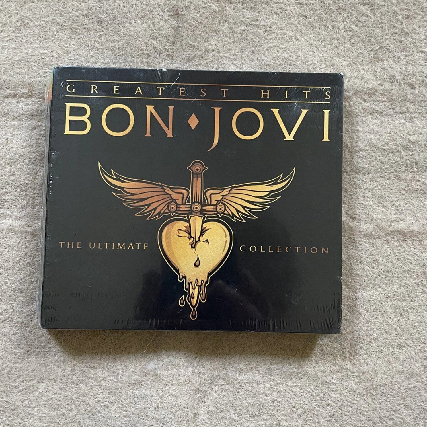 Rock Music CD Album with Bold Black & Gold Art Cover, Eye-Catching Sword-Heart-Wings Logo + High-Energy Rock TracksC Qme Greatest Hits