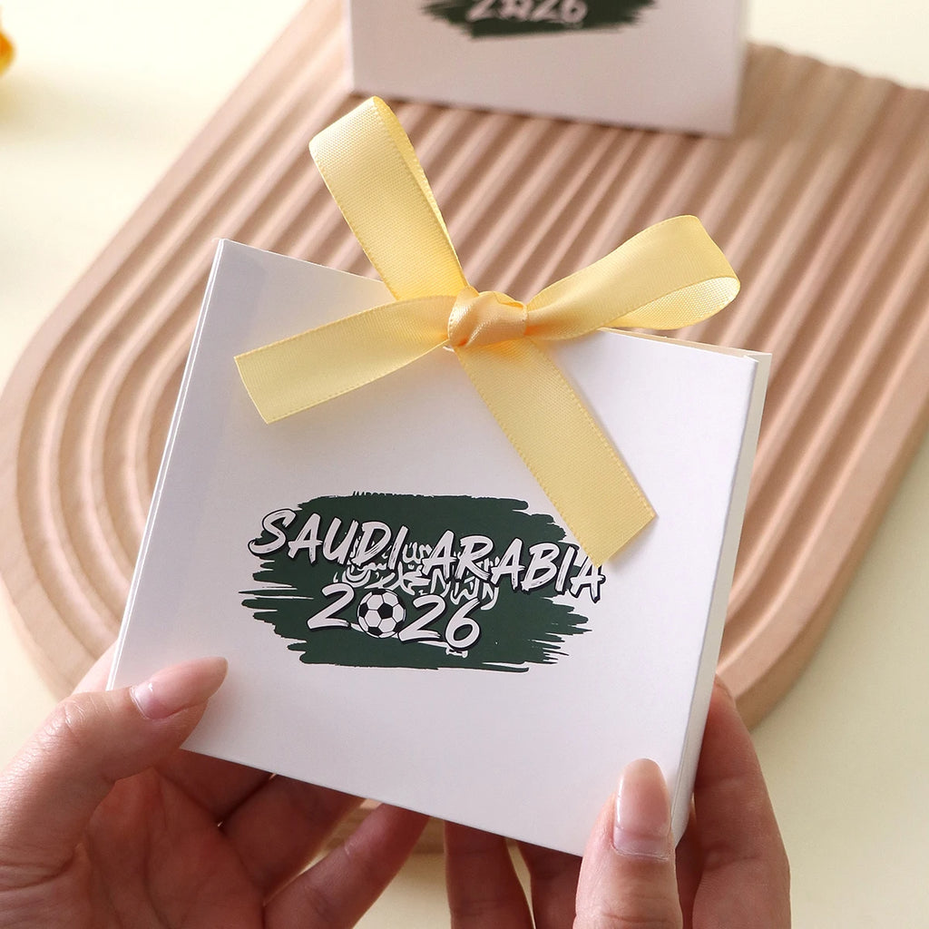 Saudi Arabia 2026 Football-Themed Gift Box, Simple White Box with Green Football Print, Adorned with a Delicate Yellow Satin Ribbon Bow, Featuring a Clean and Elegant Design The Box Has Clear Printing and a Fine Texture, Maki Qme