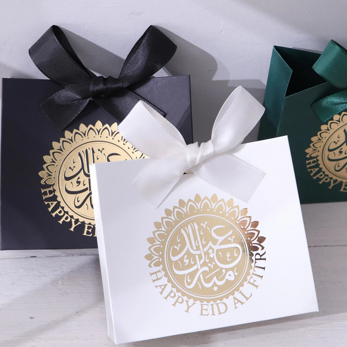 5 Exquisite and Compact Eid Gift Boxes, Each Featuring Elegant Black, Luxurious Green, and Pure White as Their Main Colors, Adorned with Delicate Arabic Script and Golden Circles, and Tied with Luxurious Gold and Silver Ribbo Qme