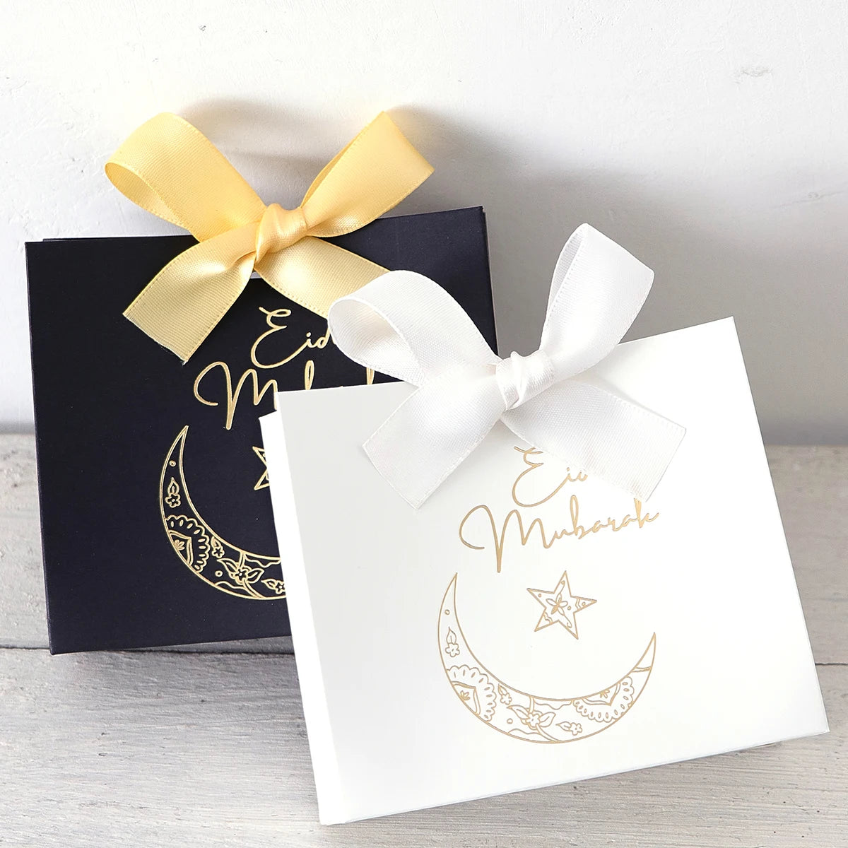 5 Exquisite and Compact Eid Gift Boxes, Available in Elegant Black, Luxurious Green, and Pure White, Decorated with Delicate Gold and Silver Star and Moon Patterns, and Adorned with Luxurious Gold and Silver Ribbons. These Gi Qme